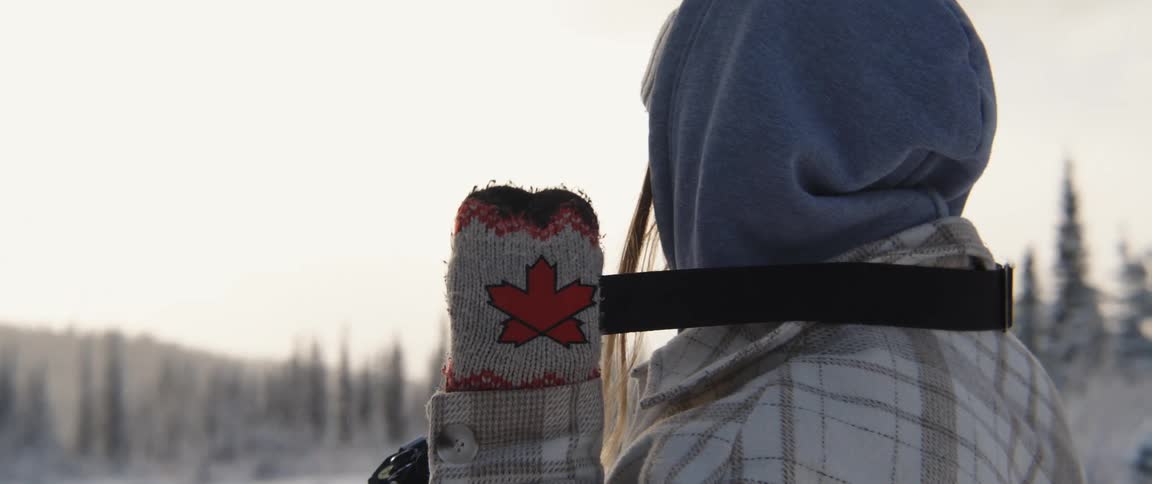 Woman wearing winter clothes takes a strapped camera over her shoulder in front of a forest