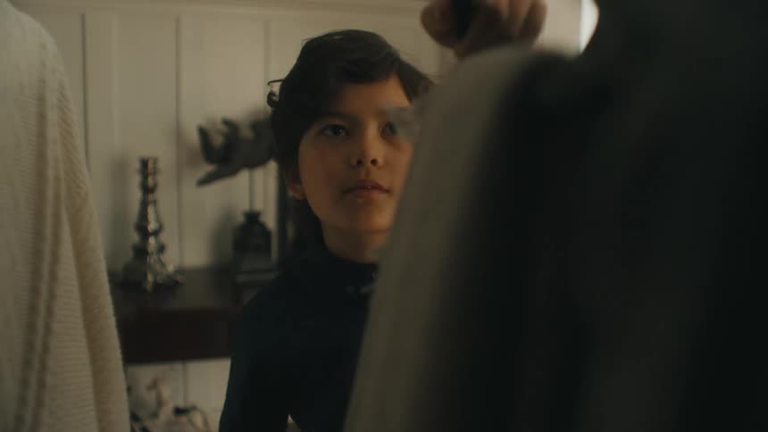 A young boy in a store takes a scarf off of a rack to look at the price tag