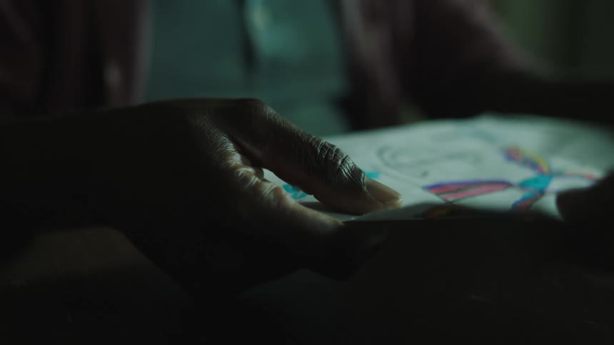 Man sitting at a table inside a dimly lit room holding a drawing on a sheet of paper