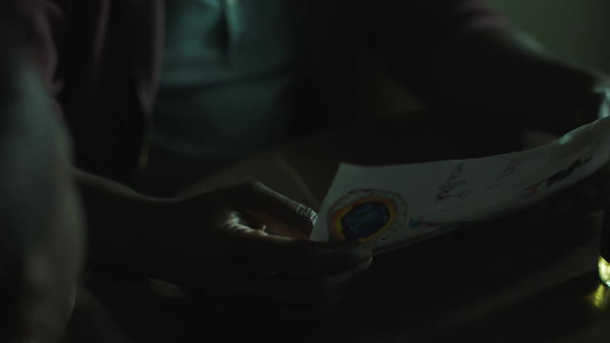 A black child is at a table finger painting and gives the picture to an adult at the table