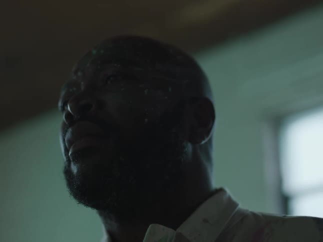 A black man wearing a white shirt is in a room looking around