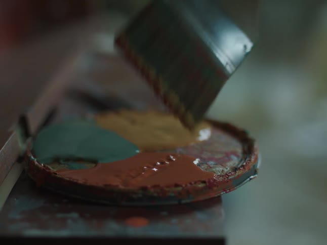A brush is dabbed into the red paint on a can cover
