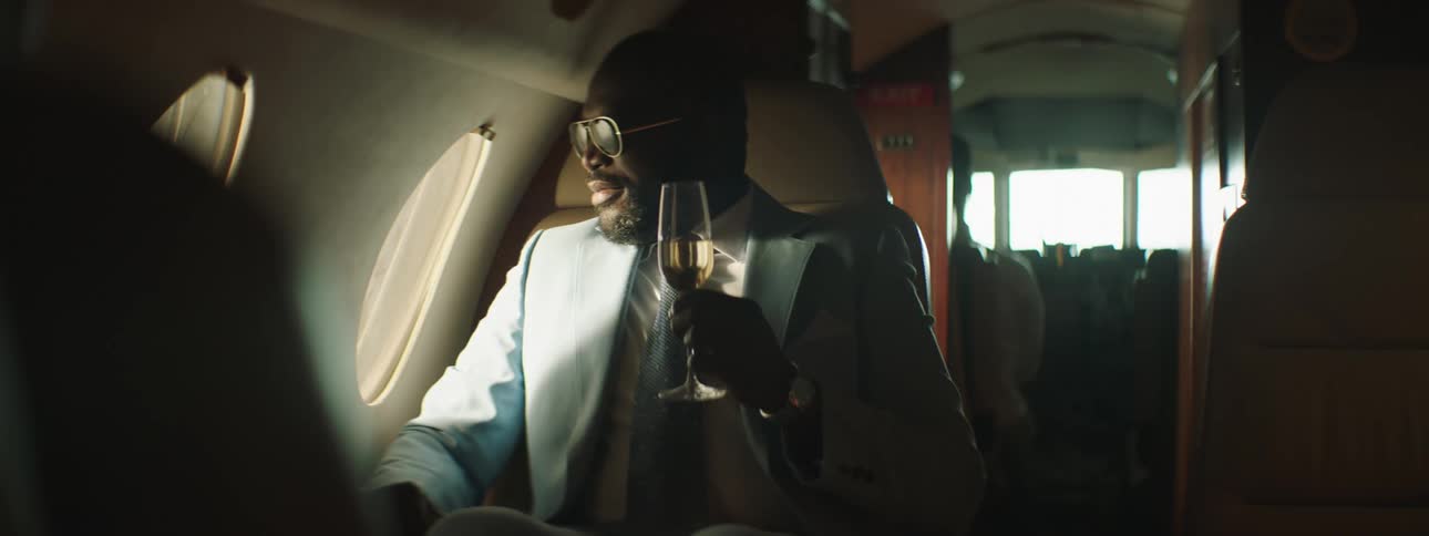 Man wearing suit sits in back of private jet holding a wineglass