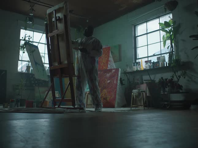 A man is standing in an art room and painting on a canvas