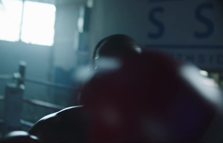 Strong muscular man inside a ring on a dimly lit gym boxing at the camera