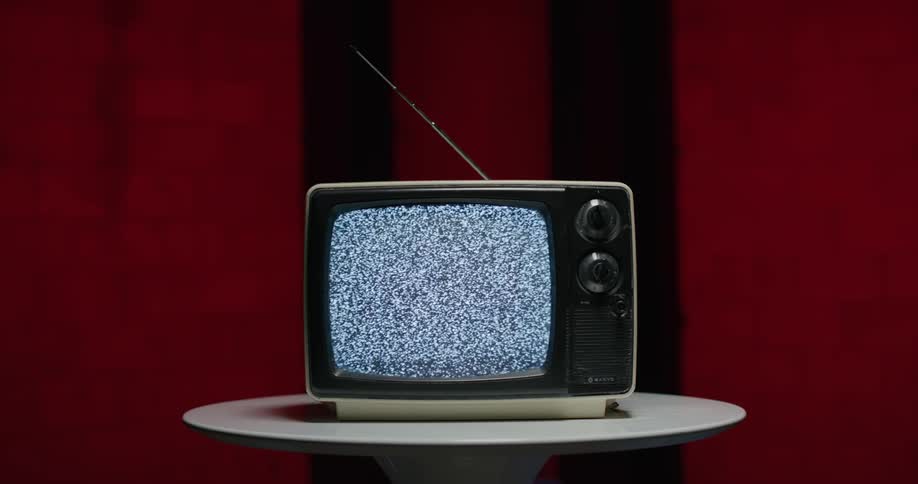 A small old television with antenna sits on a round table top playing static
