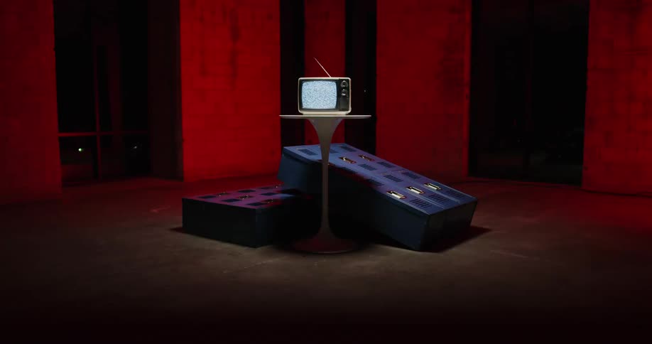 A strobe light flashes on a portable television sitting on a table and two mattresses on the floor in a room with red walls