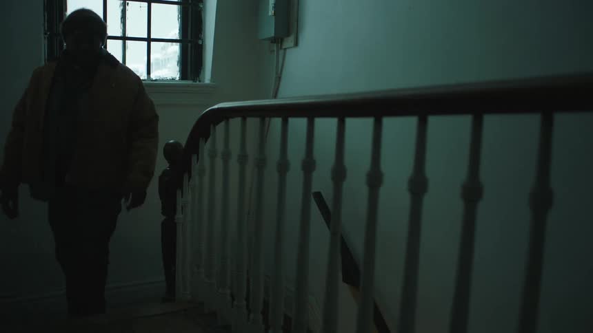 Man wearing winter clothes climbing the staircase inside a dimly lit home