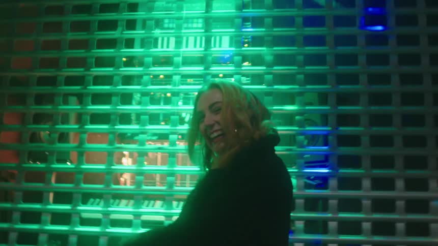 Young woman dancing and modelling under the colorful lights outside a closed store at night