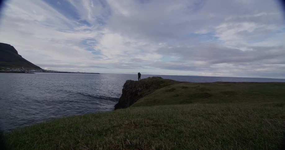Two people hike to the edge of a cliff near the water