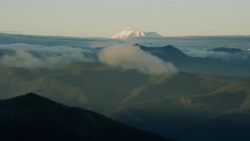 Dynamic aerial perspective of Cascade Range and Mount St Helens at sunset with clouds both in foreground and background