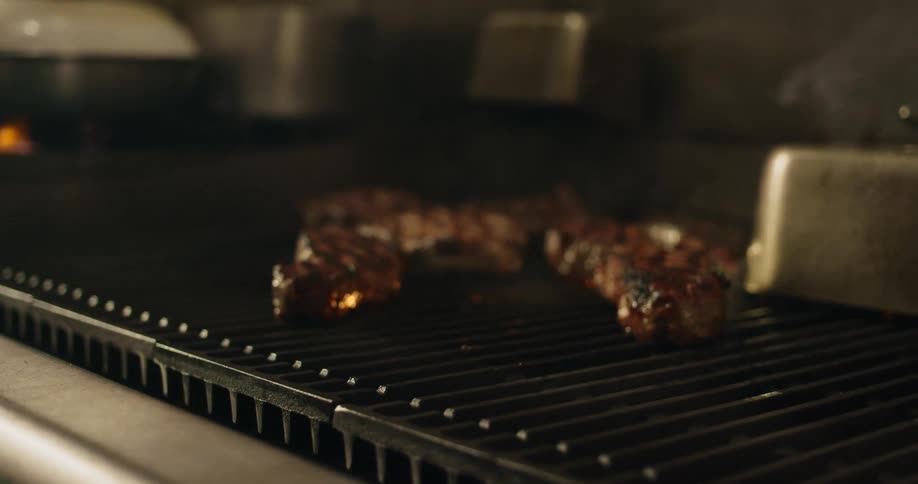 Someone is cooking steak on a grill and the flames are flaring up