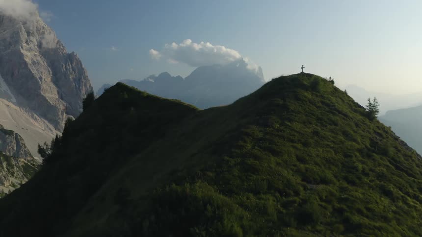 A man walks on a sloped hill leading to a cross on a mountain