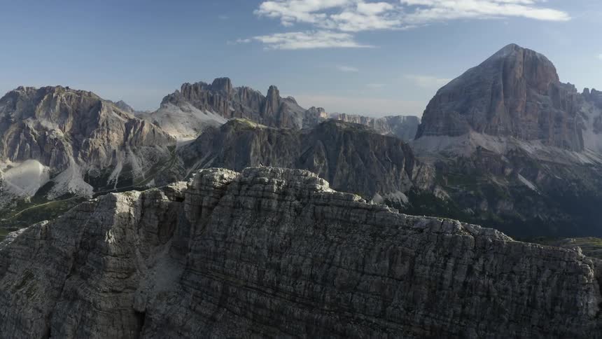 Person stands on ridge on top ofstony mountain looking over valley toward other mountains