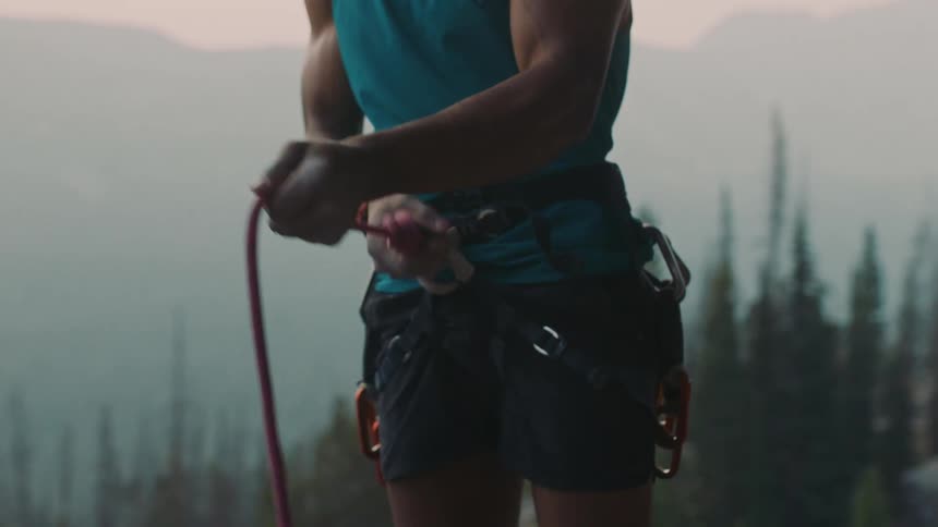 A man wearing shorts is tying a rope to a belt around his waist