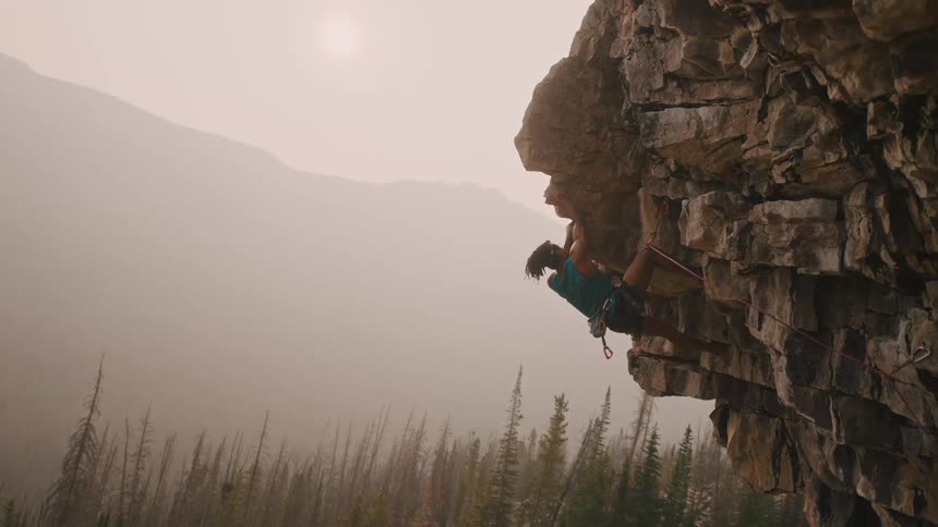 Heavy fog obscures forest mountain and sun as man rock climbs jagged cliff side
