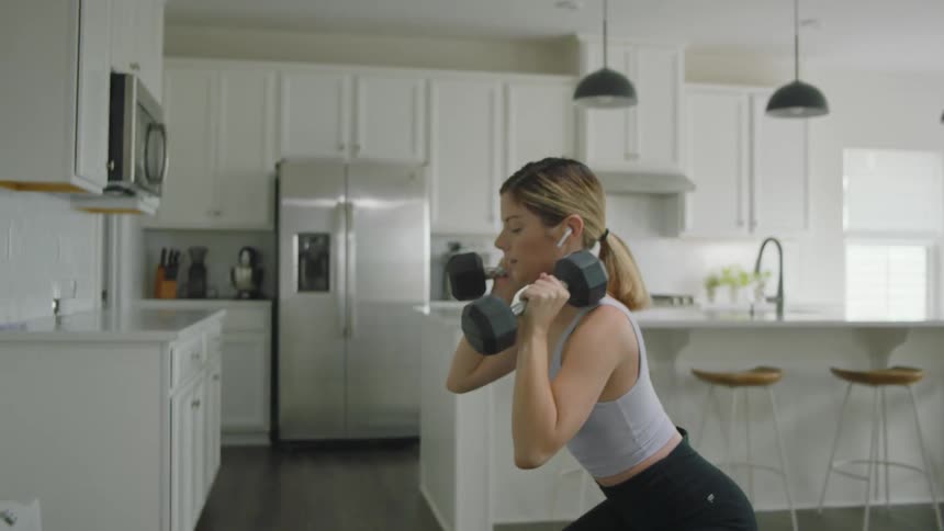 Young fit woman working out with weights on the kitchen at home