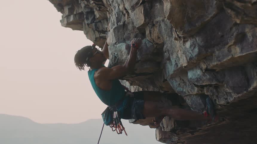 Young man wearing mountaineering gear climbing a escarpment on the side of a mountain