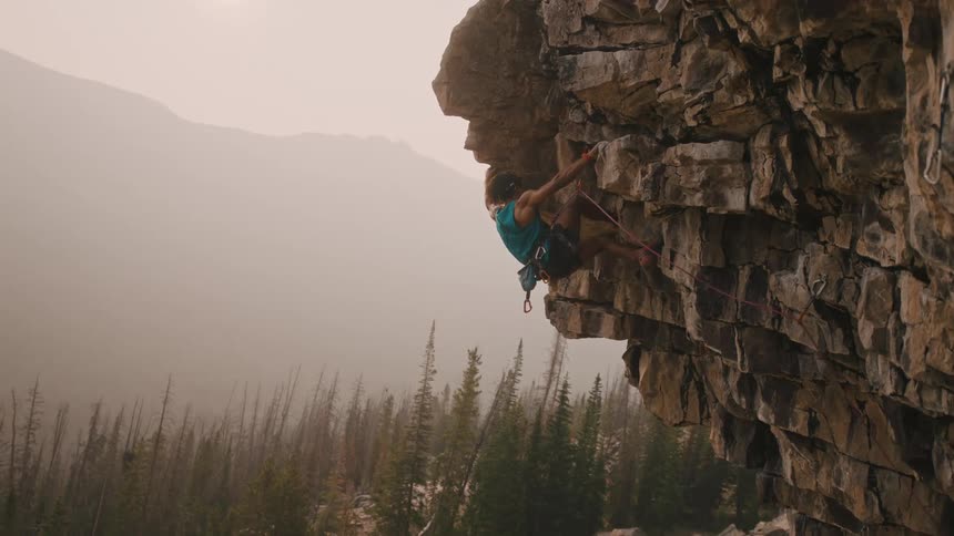 A man is climbing up a steep cliff along the side of a mountain