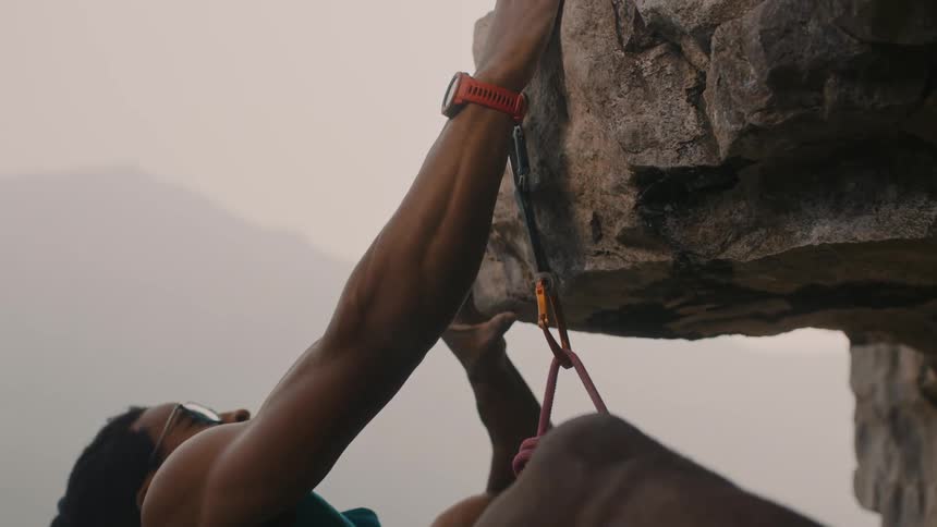A man climbing up the side of a mountain pulls himself up
