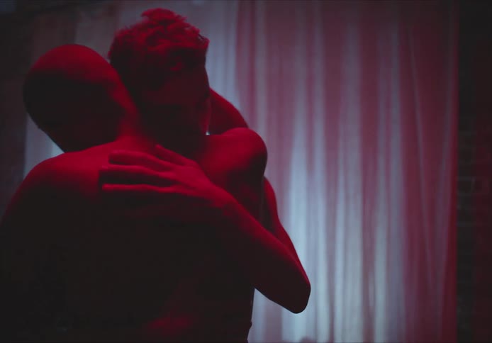 Two men slow dance in living room dimly lit by red light