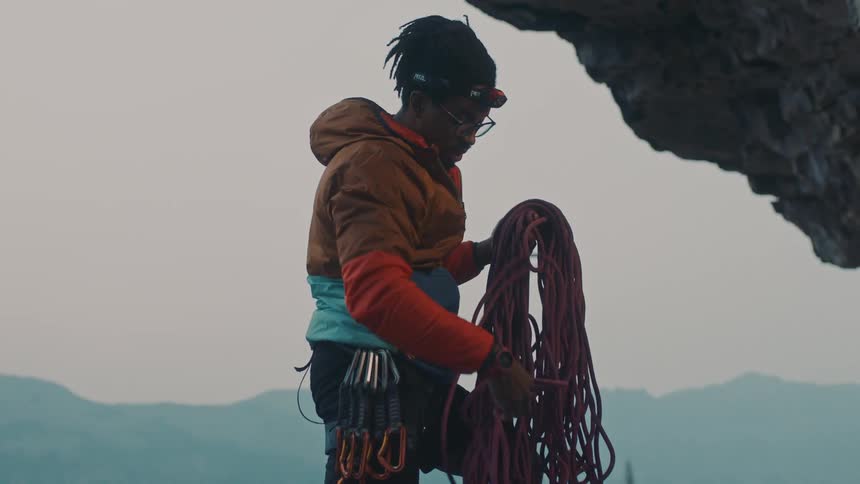 Young man wearing mountaineering gear untangles a rope near a cliff in the mountains