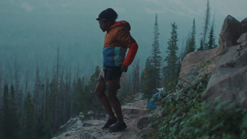 A man standing on mountain ledge puts on a climbing harness