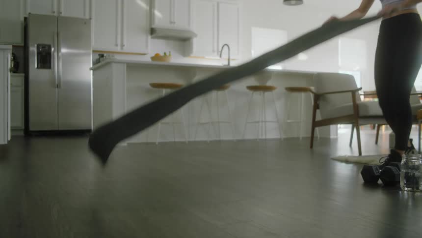 A woman at home places a yoga mat on the floor next to some weights and water