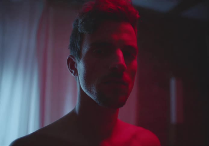 A young man stands bare chested in a home