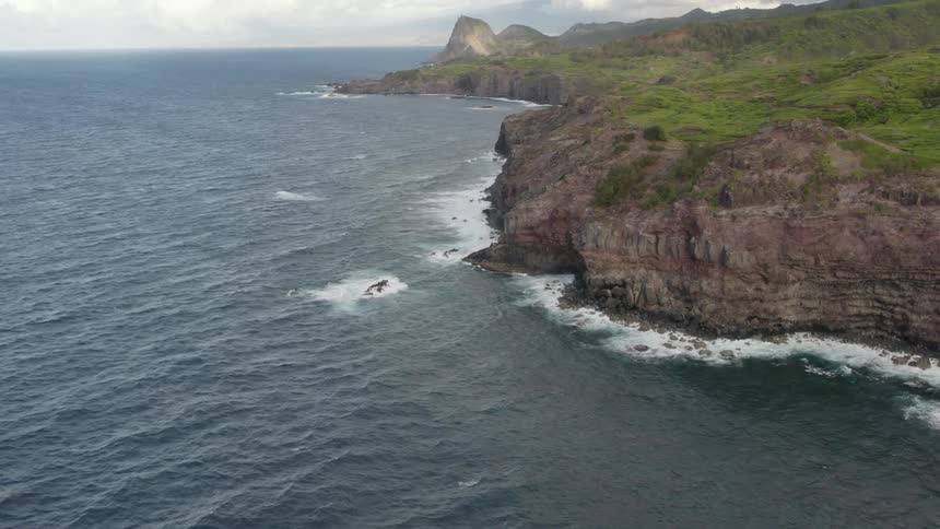 Waves crash against seaside cliffs on land stretching toward mountains