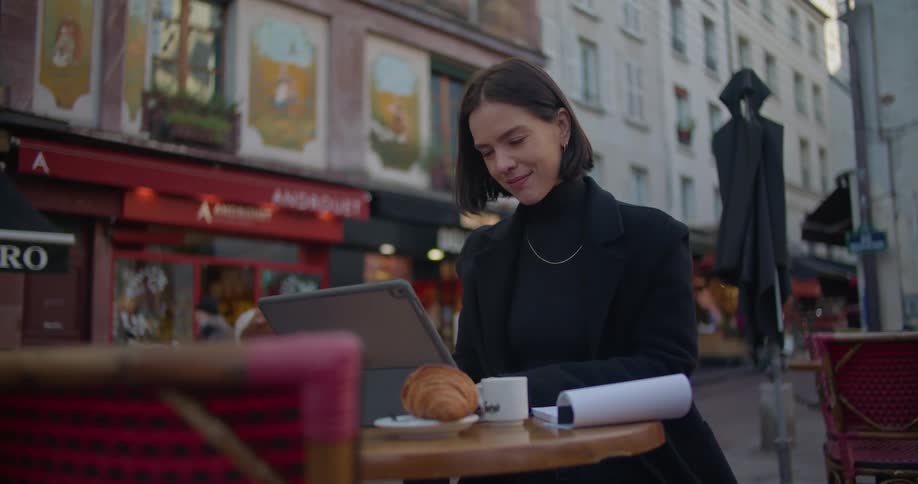 A woman is sitting at an outside table in town working on a laptop computer