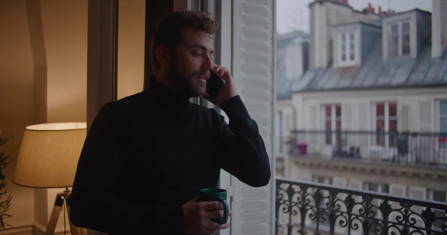 A man stands next to his apartment balcony and talks on the phone