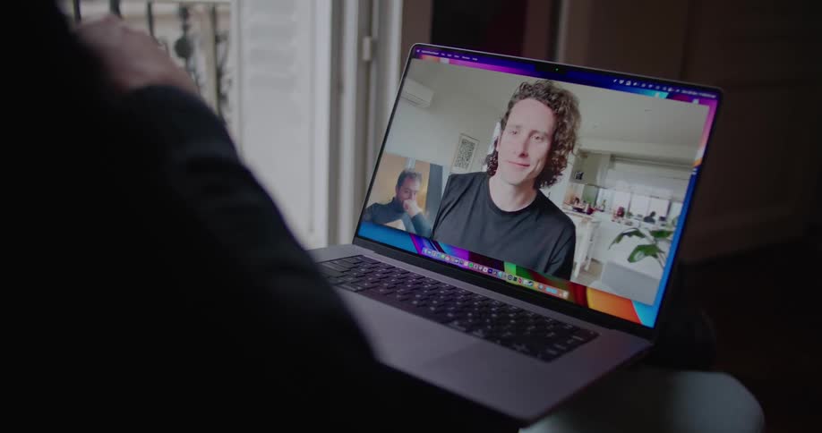 A man sitting at home with his laptop on his lap talking to another man during a video call