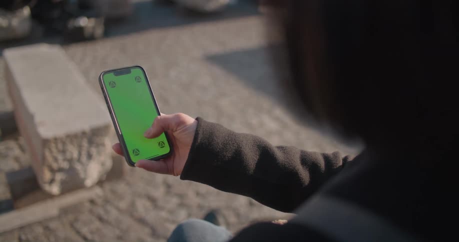 A woman scrolls through her smartphone while on a stone bench outdoors