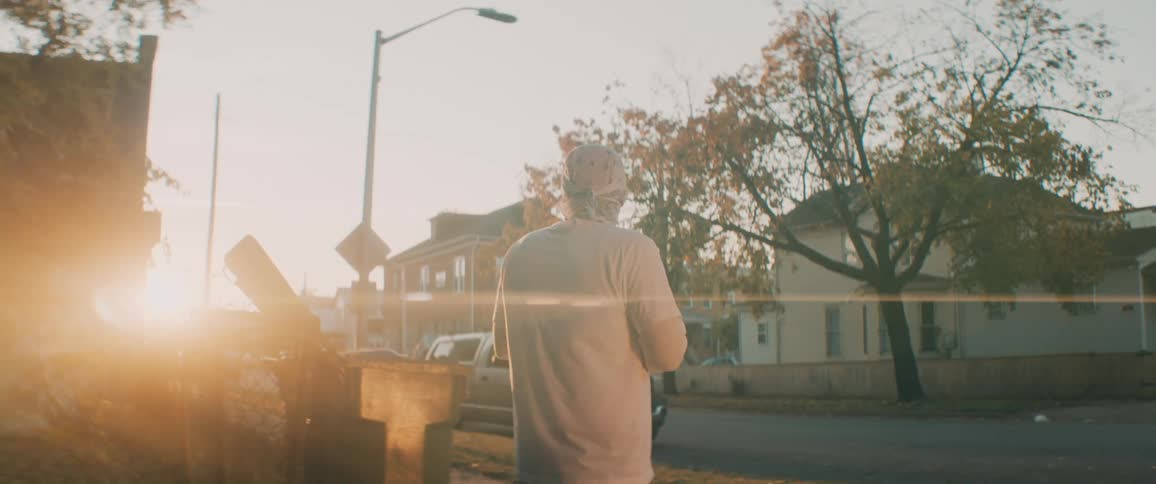 Man stands near fence looking around neighborhood as he is back lit by sun sitting near horizon