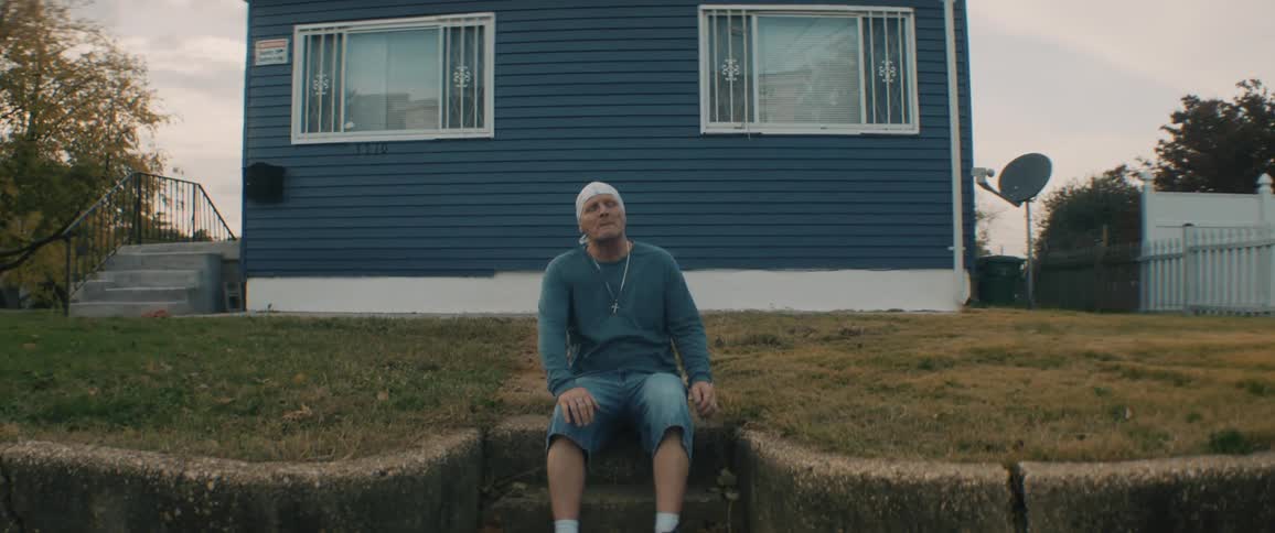 A man sits down for a portrait on steps in front of his home