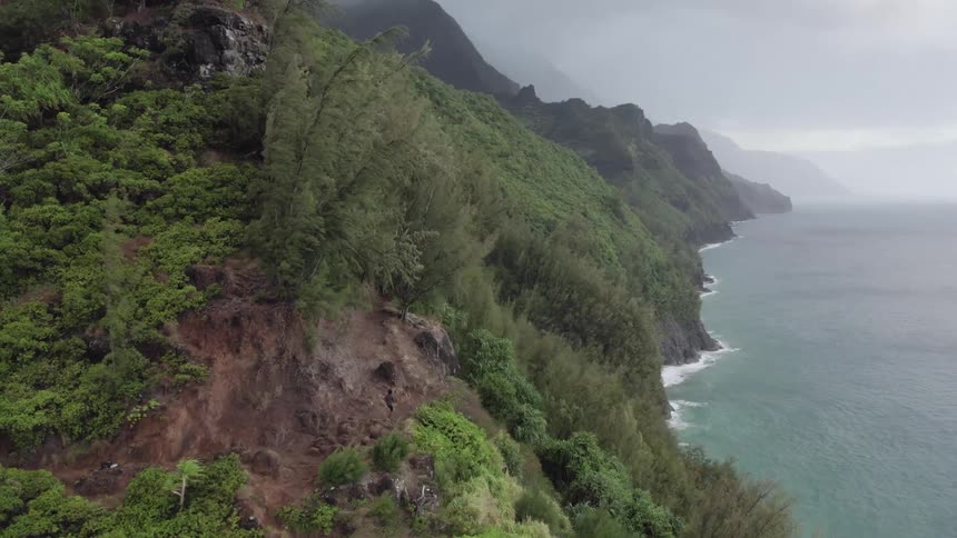 A person runs on a ridge trail on a steep slope above ocean waves