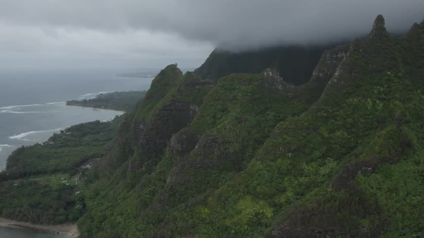 Aerial view of mountains covered on green vegetation next to the ocean under the clouds