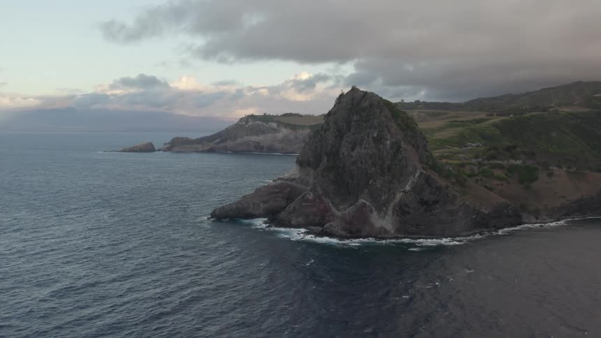 Waves crash against shore at base of mountain on misty day