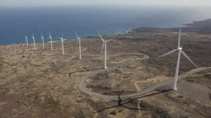 Road winds through row of wind turbines leading to the shore on misty day