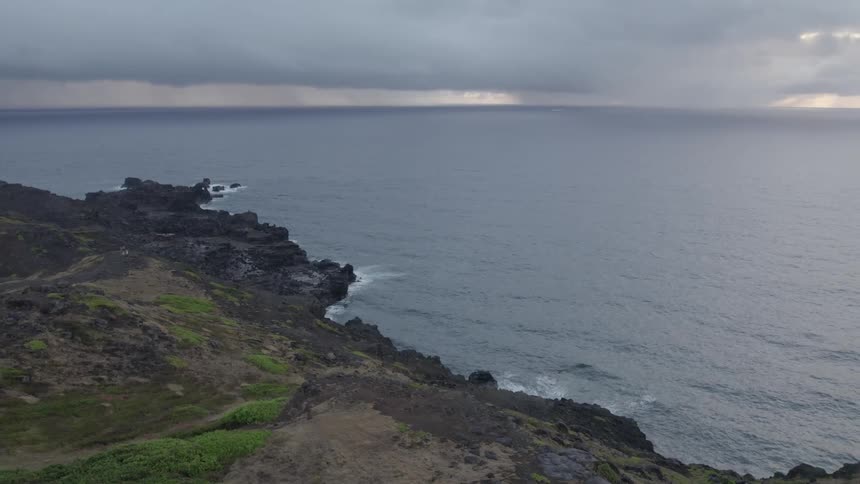 Waves roll in along the coast and crash into rocks under a cloudy sky
