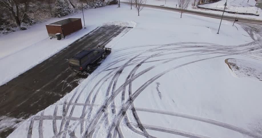 An suv with a plow attached to the front end plowing a parking lot