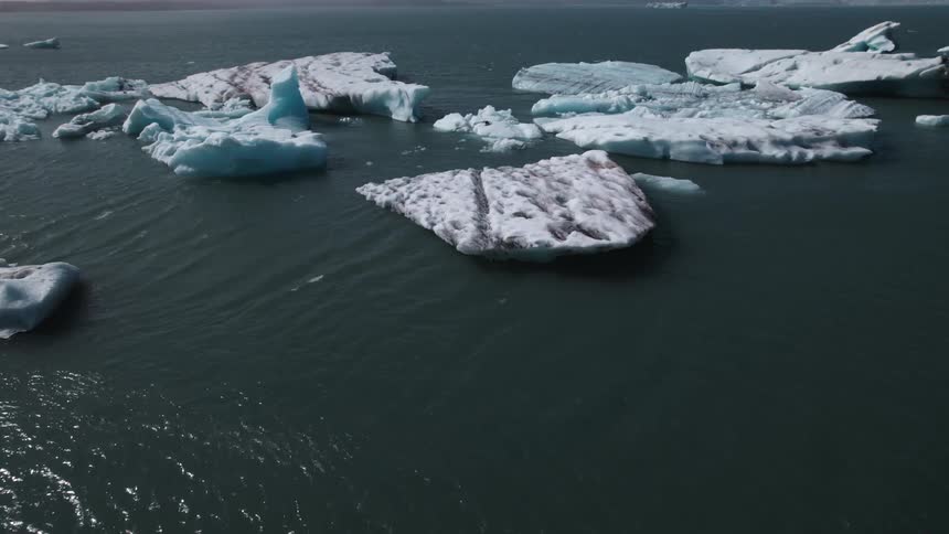 Ocean water ripples and shimmers with large pieces of ice floating near shore