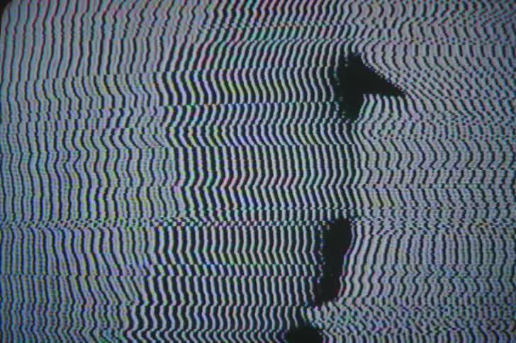 A mans face is silhouetted on a tv screen as static flashes
