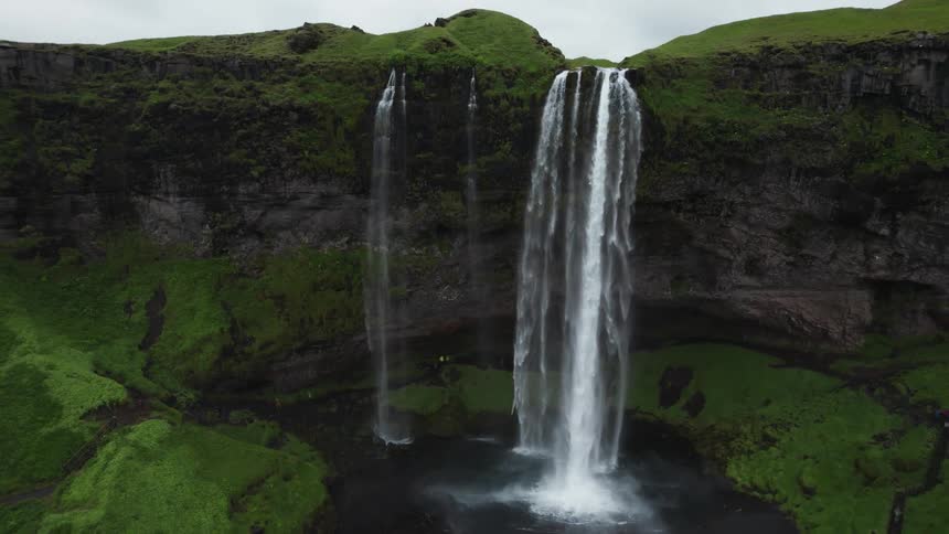 Waterfalls cascade off the side of a cliff as birds fly around it