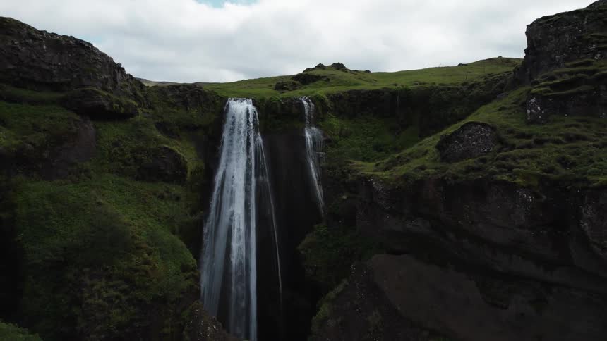 Waterfalls flow down cliff side from river running through vegetation covered plateau