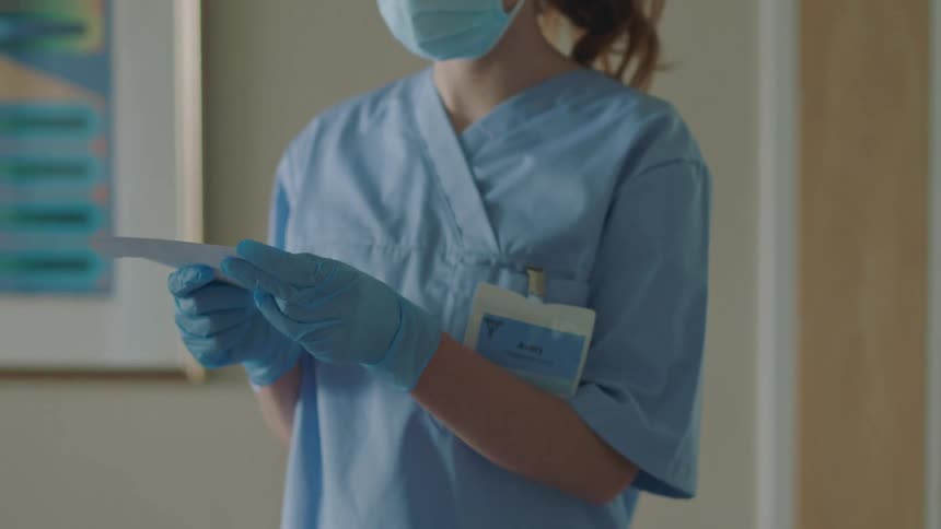 Hospital workers are busy as one worker is handed an envelope and she opens it and reads what is inside