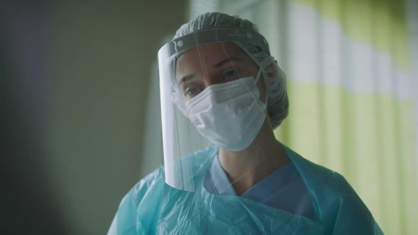 A female nurse in a face mask and shield talking to a patient