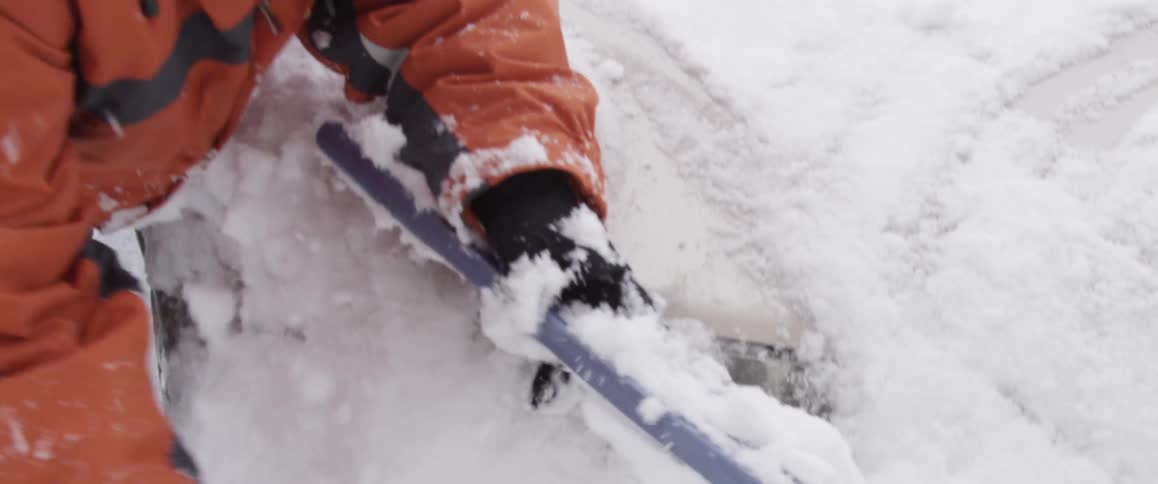 A person brushing snow off of a car