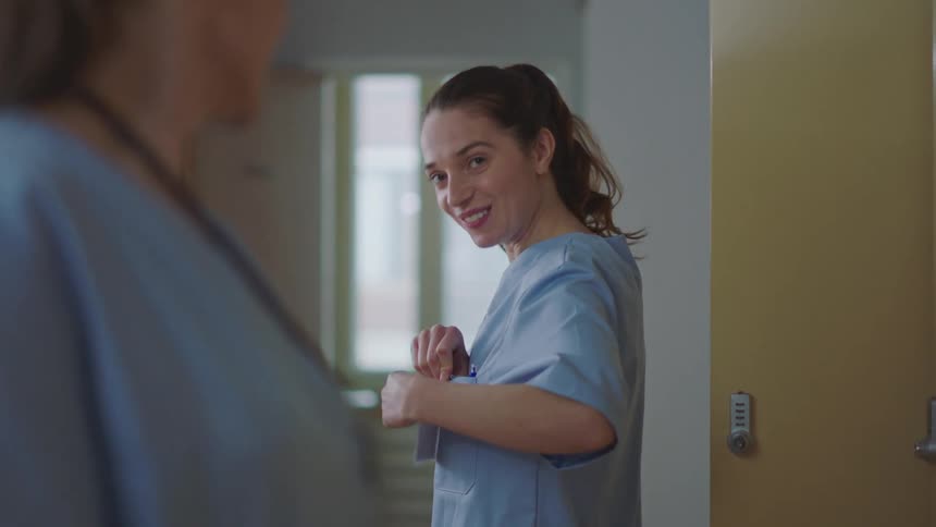 Two healthcare workers stand in a room and talk as they put their badges on